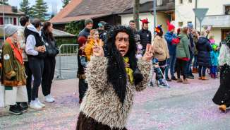 Verklede Schaanse heks bij de carnavalsoptocht in Schaan, voor publiek en kleurrijke confetti op straat