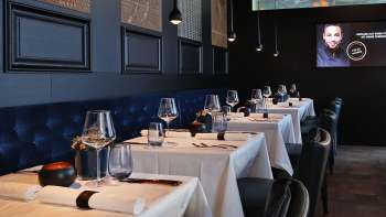 Elegant interieur van de Esquire Bar & Bistro in Vaduz met stijlvol gedekte tafels, donkerblauw gestoffeerde bank en sfeervolle verlichting.
