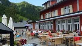 Zonnig terras van het restaurant met overdekte tafels, parasols en uitzicht op de Alpen.