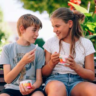 Twee kinderen zitten op een bankje in het park in Liechtenstein en eten een ijsje - lachende gezichten, bloemen en een zomerse sfeer op het platteland