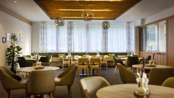 Een andere hoek van de eetruimte, met dezelfde ronde tafels, een gezellige sfeer en moderne verlichtingsinstallaties.