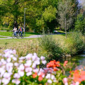 Fietsers genieten van het zonnige weer langs de met bloemen omzoomde oevers van het Haberfeld Natuurpark.