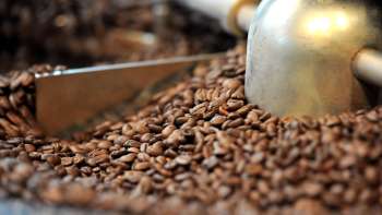  Close-up van vers gebrande koffiebonen in een brandmachine met op de achtergrond een metalen schep en een brandtrommel die de koffie mengt.