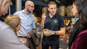 Een medewerker legt brouwingrediënten uit aan een groep geïnteresseerde gasten tijdens een rondleiding door de brouwerij.