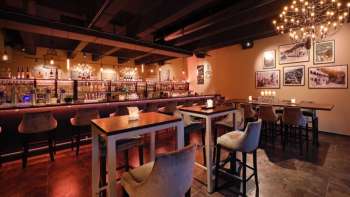 Elegant restaurantinterieur met donkerhouten elementen, bargedeelte en comfortabele stoelen in een gezellige sfeer.