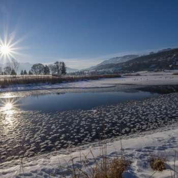 Zonsopgang bij het Egelmeer in Mauren in de winter met glinsterend ijs, sneeuw en een zonnige bergachtergrond.