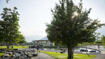 Zonnige wandeling met schaduwrijke bomen en uitzicht op het water bij Recreatiecentrum Grossabünt in Ruggell.