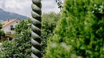 Renaissance kunstwerk van Daniel Spoerri met opvallende zuilvorm en bronzen figuur, midden in de natuur in Liechtenstein.