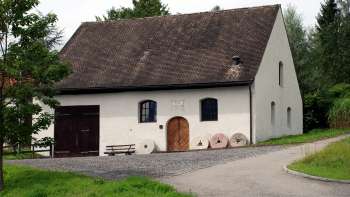 Traditionele molen in Eschen met een witte gevel, donkere luiken en een oud molenstenen ensemble voor de ingang - omgeven door groene weiden en bomen.
