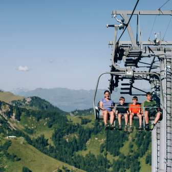 Gezin met kinderen op een stoeltjeslift boven de groene bergen van Malbun - zomeravontuur en panoramisch uitzicht in Liechtenstein