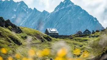 Uitzicht op de Pfälzerhütte, gelegen op een groene alpenweide tegenover steile rotswanden in de Liechtensteinse Alpen.