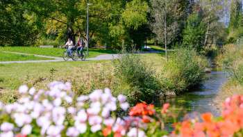 Fietsers genieten van het zonnige weer langs de met bloemen omzoomde oevers van het Haberfeld Natuurpark.