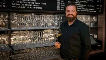 Vriendelijke barman van de WY Weinbar met wijnglas voor een stijlvol schap vol glazen en wijnen.