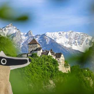 Uitzicht op Kasteel Vaduz met detectieven-trail op de voorgrond en besneeuwde Alpen op de achtergrond.