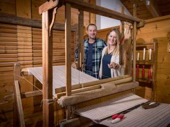 Een stel bekijkt een werkend historisch weefgetouw in het Walser Museum Triesenberg in Liechtenstein, omringd door houten lambrisering