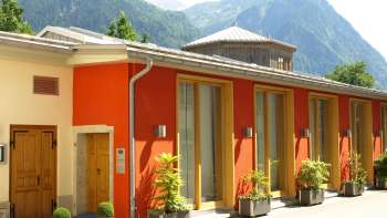 Buitenaanzicht van het Cultureel Centrum Gasometer met kleurrijke gevel en Alpenpanorama op de achtergrond.
