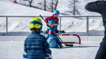 Schaatsende familie in Malbun, kind zittend op een diervormige schaatshulp.