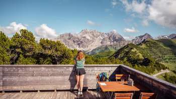 Vrouw geniet van het panoramische uitzicht op de omliggende bergen vanaf het terras van het bergrestaurant Sareis