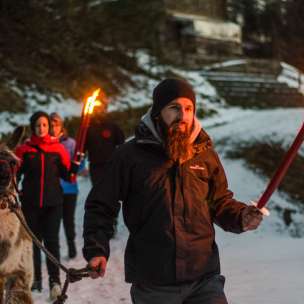 Groep op een begeleide lamawandeling in het besneeuwde Liechtenstein met fakkels - sfeervol outdooravontuur voor jong en oud.
