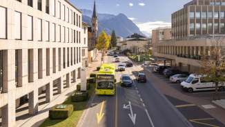 Een LIEmobil-bus rijdt door Vaduz tegen de achtergrond van de Alpen en moderne architectuur