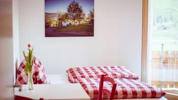 Gezellige tweepersoonskamer in het pension op Camping Mittagsspitze met rood en wit geruit beddengoed en decoratie.