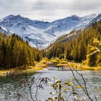 Herfstsfeer in Steg, Liechtenstein, met kleurrijke bossen, een helder meer en besneeuwde Alpen op de achtergrond
