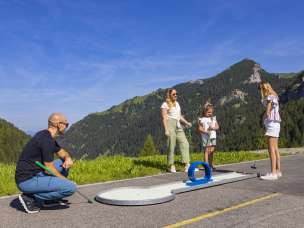 Een gezin geniet in de zomer van een partijtje minigolf in het zonnige Malbun in Liechtenstein, omringd door een groen Alpenlandschap en bergen.