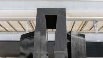 Sculptuur "Progression of a Form in 3 Stelae" van Christian Megert gemaakt van zwarte steen voor een moderne glazen gevel in Vaduz.