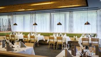 Een uitnodigende eethoek met ronde tafels en zachte groene stoelen, ingericht in een moderne, natuurlijke stijl.