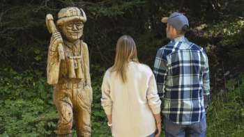 Wandelaars bekijken gebeeldhouwde houten figuren langs de "pad van de Walser legendes"