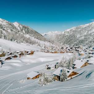 Luchtfoto van Malbun in de winter met besneeuwde houten huizen, genesteld in het Liechtensteinse Alpenlandschap