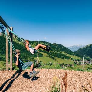 Twee kinderen schommelen op een speelplaats in de bergen met uitzicht op het zomerpanorama van Malbun in Liechtenstein