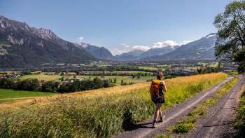 Vrouw wandelt over een onverharde weg met een panoramisch uitzicht over de Rijnvallei in Liechtenstein