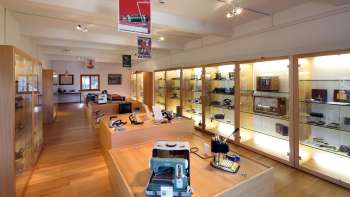 Uitzicht in een lichte tentoonstellingsruimte van het Lawena Museum met verlichte vitrines vol historische elektrische apparaten.