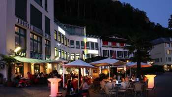 Avondsfeer voor Brasserie Burg in Vaduz met verlicht terras en gasten onder parasols.