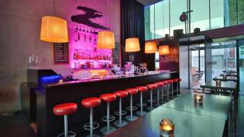 Moderne bar met lange toonbanken, rode barkrukken en stijlvolle verlichting in roze en oranje