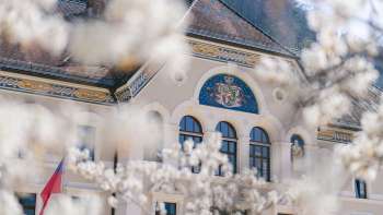 Regeringsgebouw van Vaduz omlijst door bloeiende bomen in de lente, met de focus op het nationale wapen.