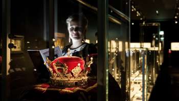 Vrouw kijkt naar de prinselijke hoed in de Schatkamer van Liechtenstein, omringd door verlichte vitrines.
