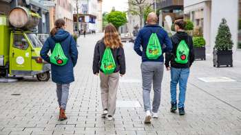 Vier jongeren met groene FoodTrail-rugzakken wandelen door het centrum van Vaduz Vier jongeren met groene FoodTrail-rugzakken wandelen door het centrum van Vaduz