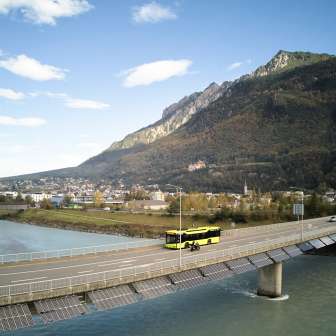 Gele LIEmobil-bus rijdt over de Rijnbrug bij Vaduz met een bergpanorama op de achtergrond - Beleef Liechtenstein
