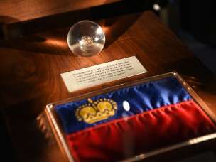 Tentoonstelling in de Schatkamer van Liechtenstein: Liechtensteinse vlag met gouden kroon en glazen bol met historisch artefact
