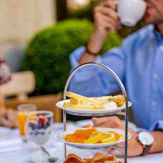 Ontbijt met worst, kaas en vers fruit op een etagère in Vaduz terwijl een gast koffie drinkt