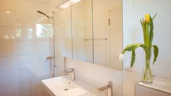 Moderne, licht betegelde badkamer in het gastenverblijf op Camping Mittagsspitze met dubbele wastafel, spiegel en verse bloemen.