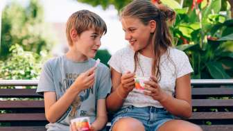 Genieten van ijs in Liechtenstein - zomerpret voor kinderen Twee kinderen zitten op een bankje in het park in Liechtenstein en eten een ijsje - lachende gezichten, bloemen en een zomerse sfeer op het platteland
