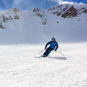 Skiërs op een brede skipiste in Malbun, Liechtenstein, omringd door besneeuwde Alpenhellingen en een helderblauwe lucht