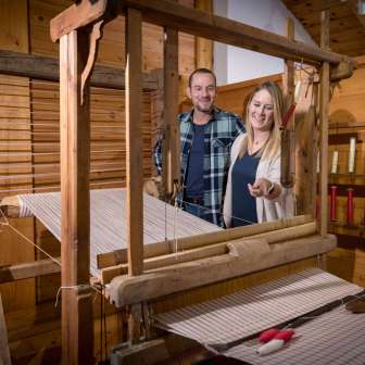 Een stel bekijkt een werkend historisch weefgetouw in het Walser Museum Triesenberg in Liechtenstein, omringd door houten lambrisering