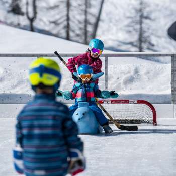 Schaatsende familie in Malbun, kind zittend op een diervormige schaatshulp.