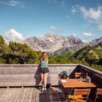 Wandelaar kijkt vanaf het houten terras bij het uitzichtplatform uit op een indrukwekkend alpenpanorama.