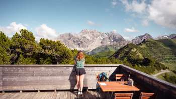 Een vrouw geniet op een heldere dag van het uitzicht op de Liechtensteinse Alpen en de Rijnvallei vanaf het uitzichtterras van Sareis