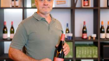 Harry Zech presenteert een fles van zijn wijn in de stijlvolle verkoopruimte - regionale wijncultuur uit Liechtenstein.